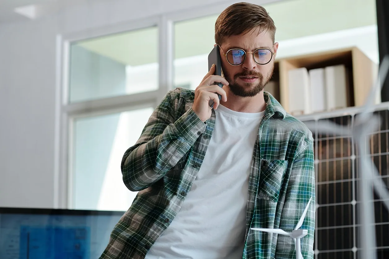 Mann in kariertem Hemd telefoniert im Büro mit Modell eines Windrads.