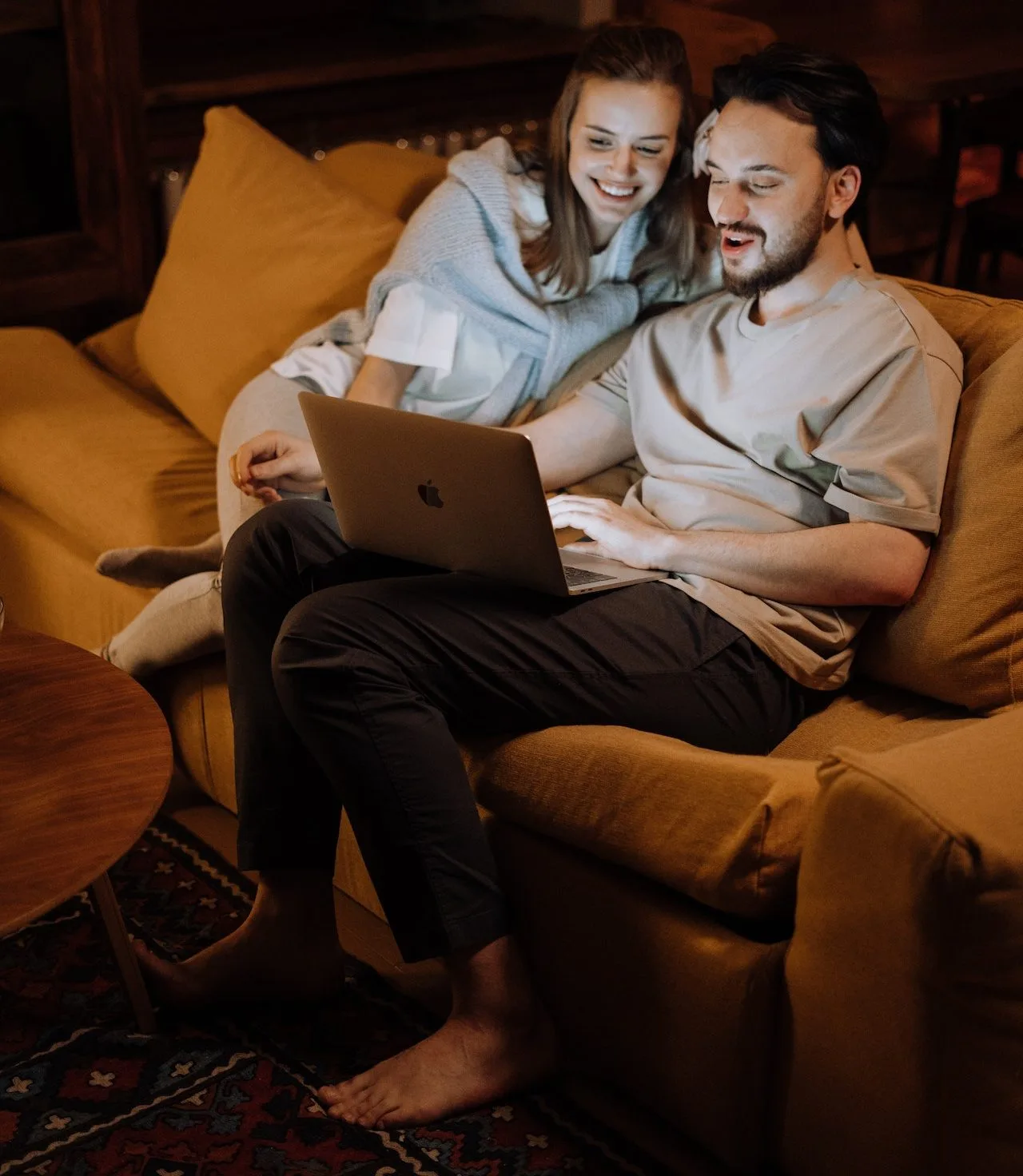 Lächelndes Paar auf Sofa, schaut gemeinsam auf einen Laptop.