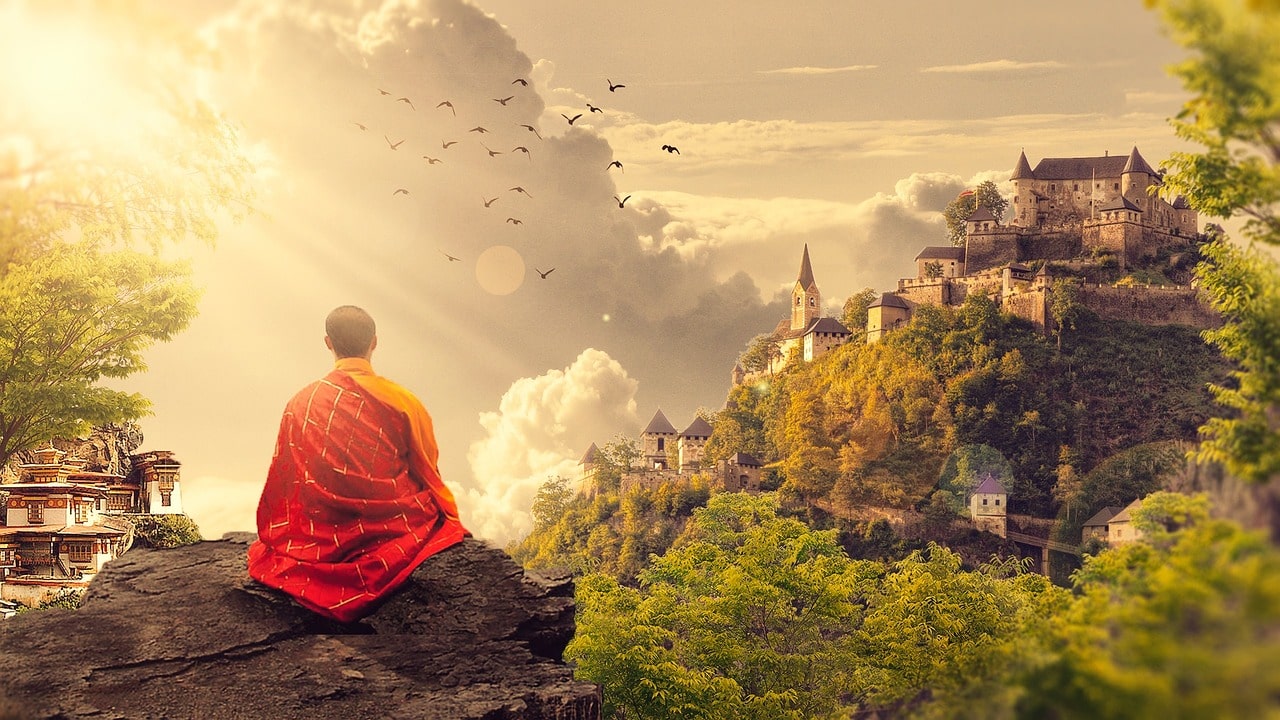 Auf dem Bild sieht man einen Mensch im Schneidersitz auf einem Berg der auf eine asiatische Landschaft blickt. Es scheint ein meditierender Mönch zu sein