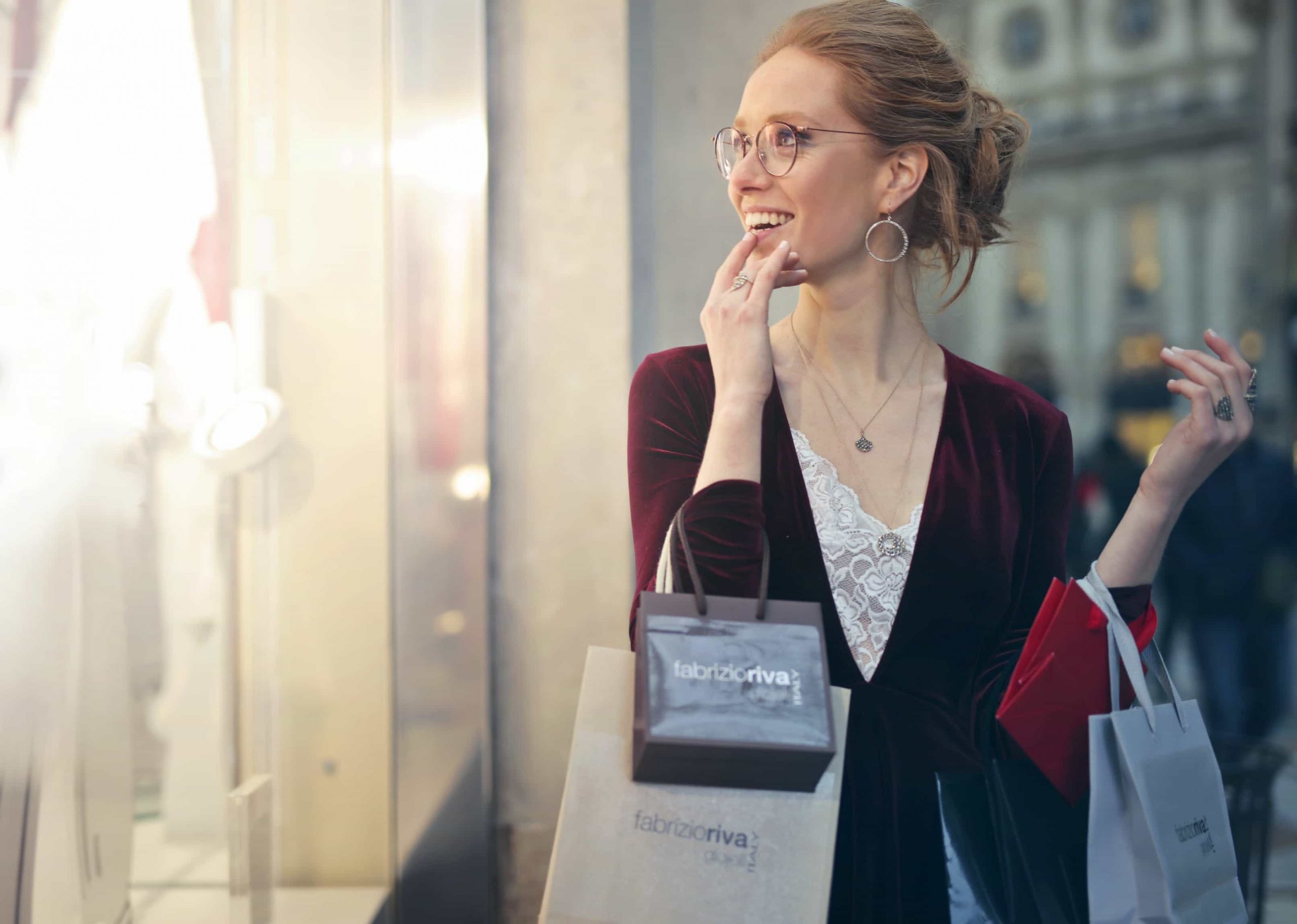 Auf dem Bild sieht man eine junge Frau mit Einkaufstüten um den Arm. Sie lächelt. Das Bild soll den Einzelhandel Salesjob andeuten.