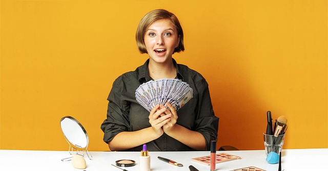 Blonde Frau in dunkelgrünem Shirt, hält viele Geldscheine in der Hand, präsentiert Kosmetik vor ihr auf dem Tisch, knallgelber Hintergrund
