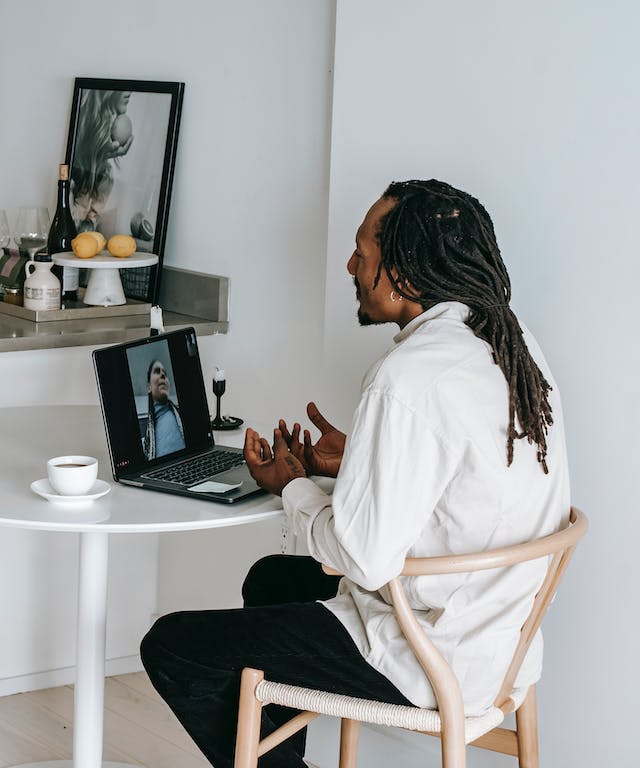 Schwarzhaariger Mann mit Rasta-Frisur sitzt vor Laptop und hält eine Videokonferenz.