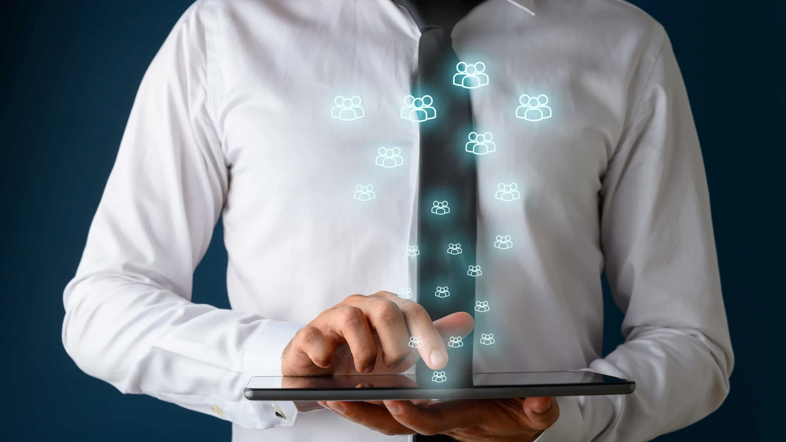 Vorderansicht eines Geschäftsmannes mit weißem Hemd und dunkler Krawatte, der ein digitales Tablet verwendet, aus dem viele leuchtende Menschensymbole herauskommen.
