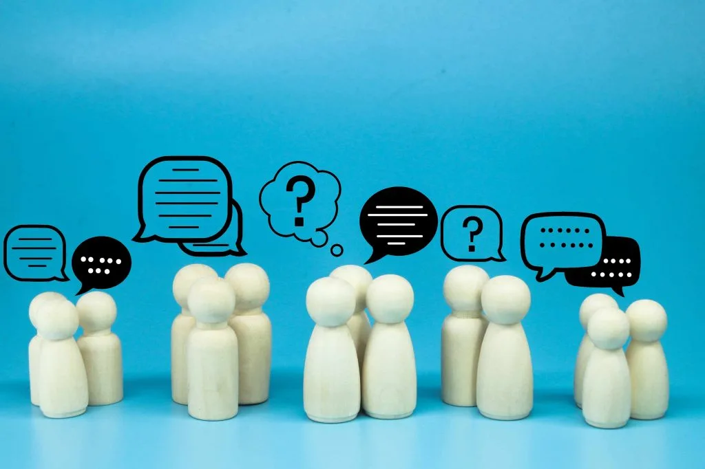 Weiße Spielfiguren in fünf Gruppen von zwei bis drei Figuren aufgeteilt. Über ihnen Sprechblasen mit verschiedenen Zeichen, das Gesamtbild stellt eine Interaktion dar. Blauer Hintergrund.