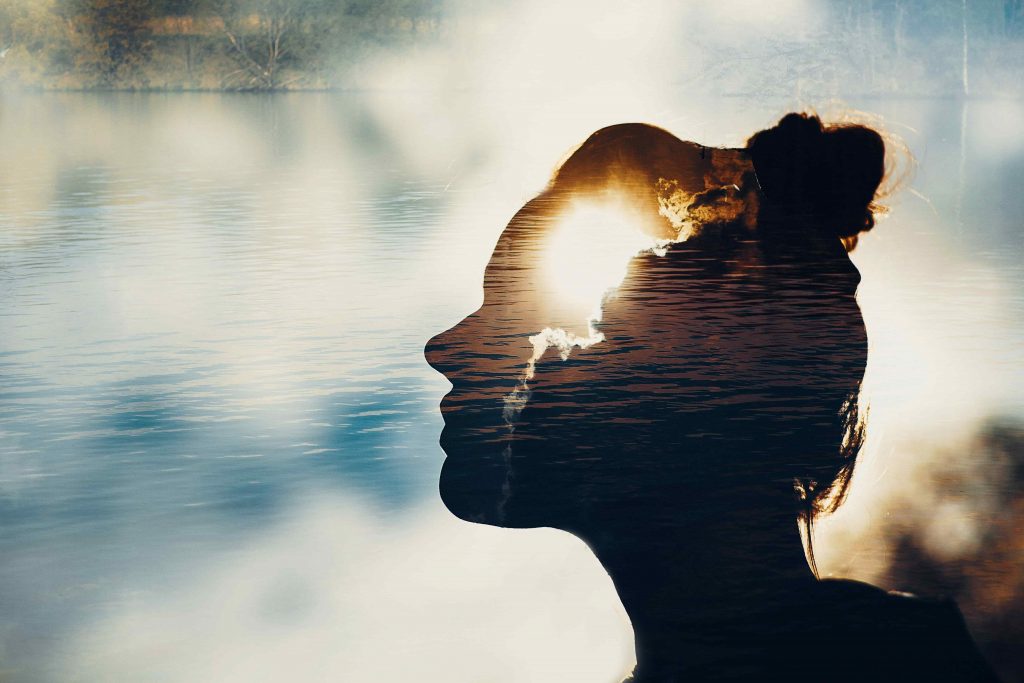 Sonne im Kopf einer Frau. Dahinter ein See.