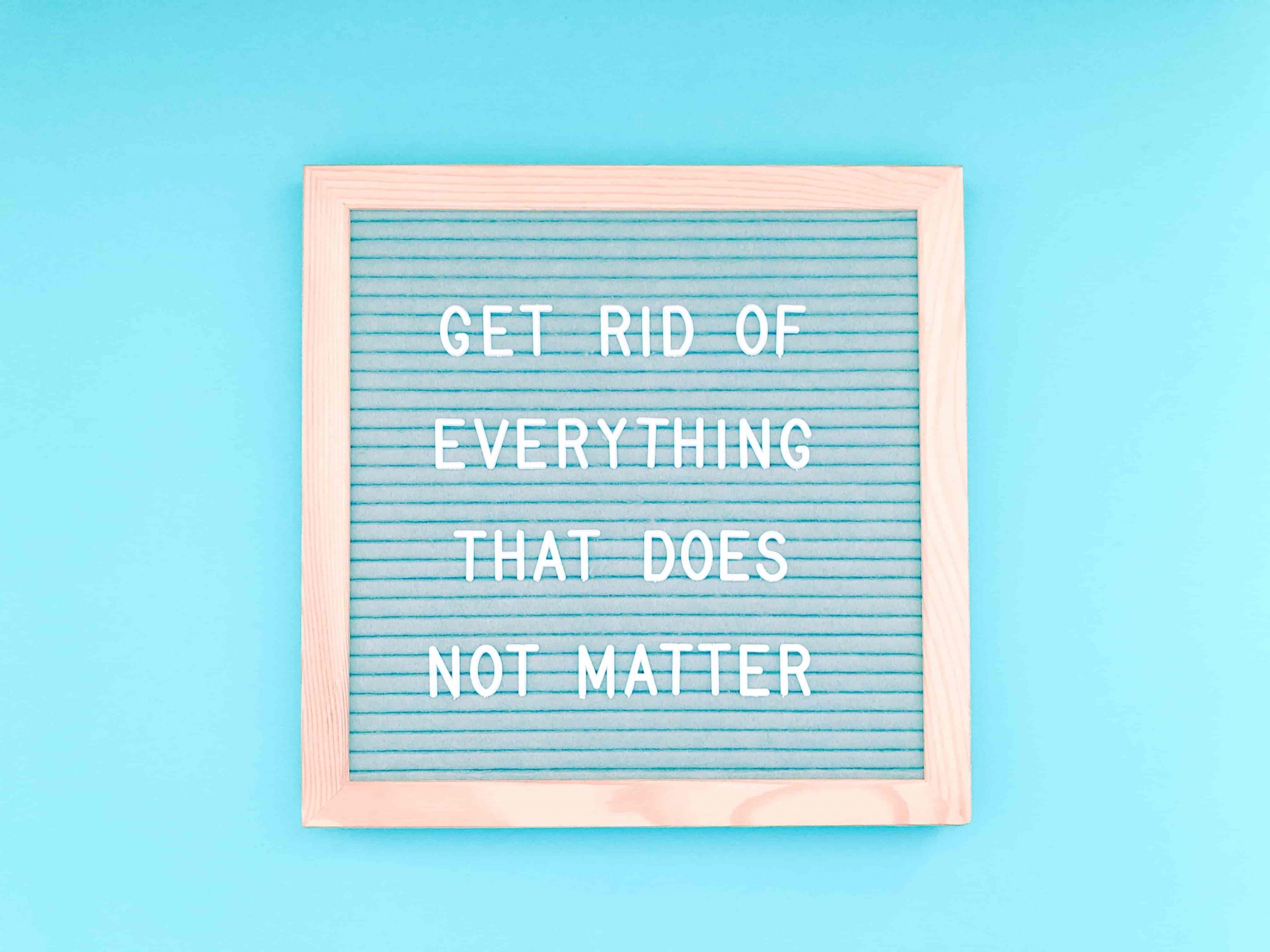 Quote in weißen Buchstaben auf blauer Tafel mit hellem Holzrand das besagt: „Get rid of everything that does not matter“. Blauer Hintergrund.