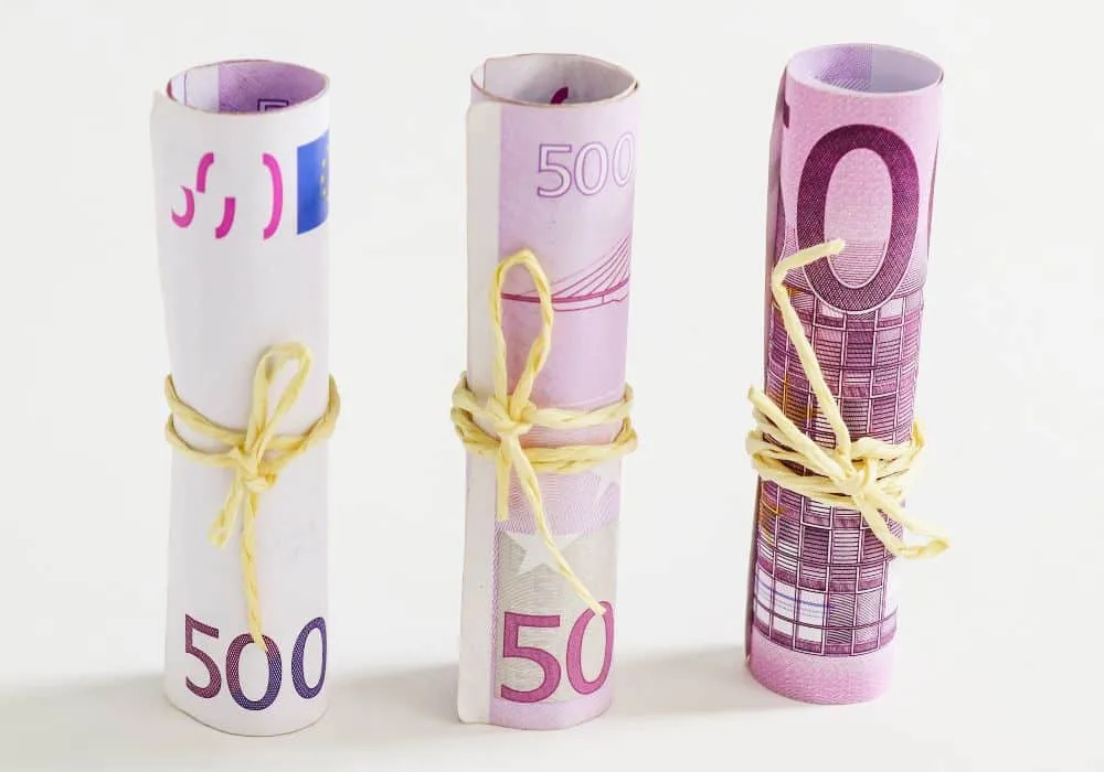 Drei 500-Euro-Scheine nebeneinander, eingerollt und gebunden. Weißer Hintergrund.