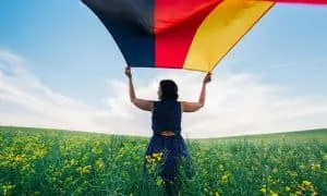 Dunkelhaarige Frau von hinten auf einer Wiese lässt eine deutsche Flagge wehen.