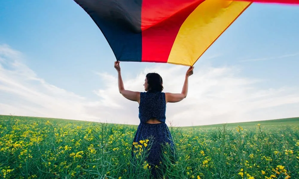 Dunkelhaarige Frau von hinten auf einer Wiese lässt eine deutsche Flagge wehen.