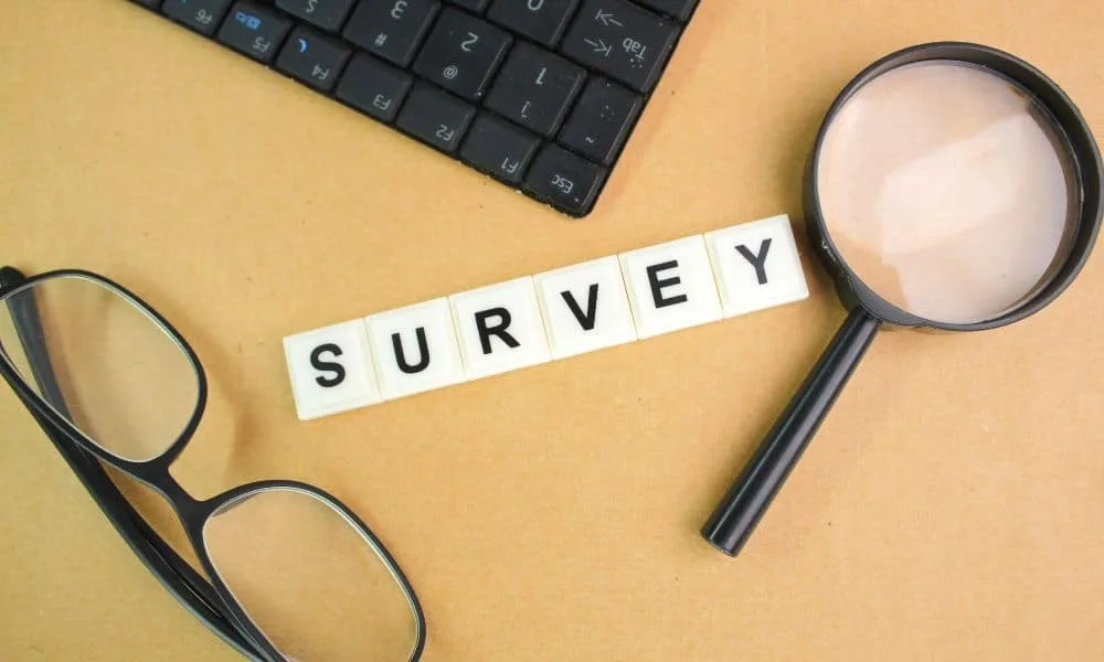 Laptop, Brille und Lupe und Würfel, die das Wort Survey bilden auf hellbrauner Platte.