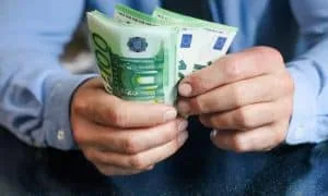 Männliche Hände in blauer Bluse halten 100 €-Scheine.