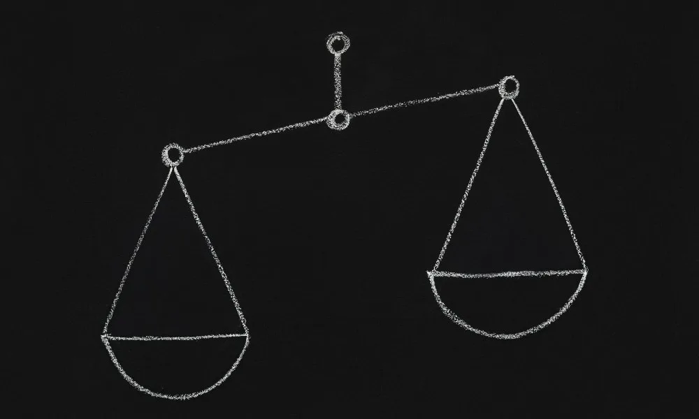 Balkenwaage mit weißer Kreide auf schwarze Tafel gezeichnet.