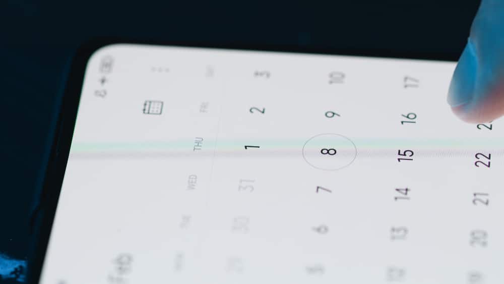 Finger tippt auf einen digitalen Kalender in Tablet. Dunkelblauer Hintergrund.