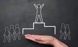 Schwarze Tafel, auf der mit weißer Kreide ein Podest mit Männchen an der Spitze gezeichnet ist. Drei Männchen auf der linken, zwei auf der rechten Seite daneben.