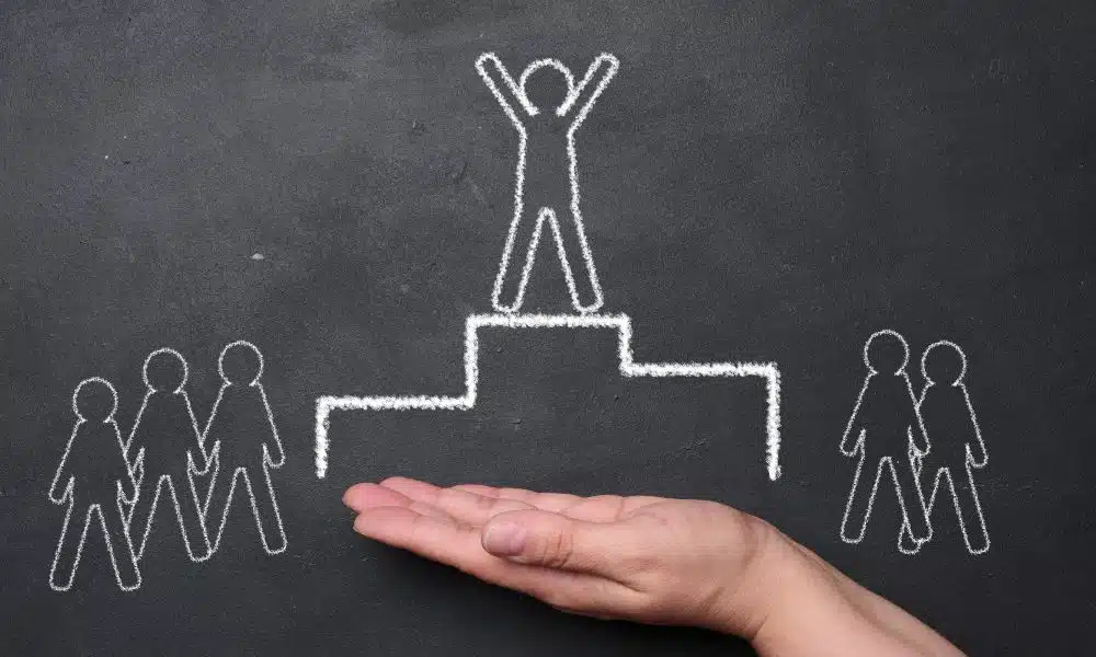 Schwarze Tafel, auf der mit weißer Kreide ein Podest mit Männchen an der Spitze gezeichnet ist. Drei Männchen auf der linken, zwei auf der rechten Seite daneben.