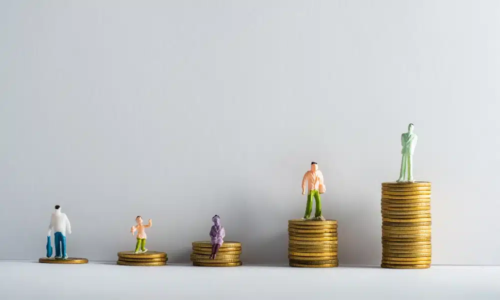 Fünf aufsteigende Münztürme, auf jedem steht eine Menschenfigur. Weißer Hintergrund.