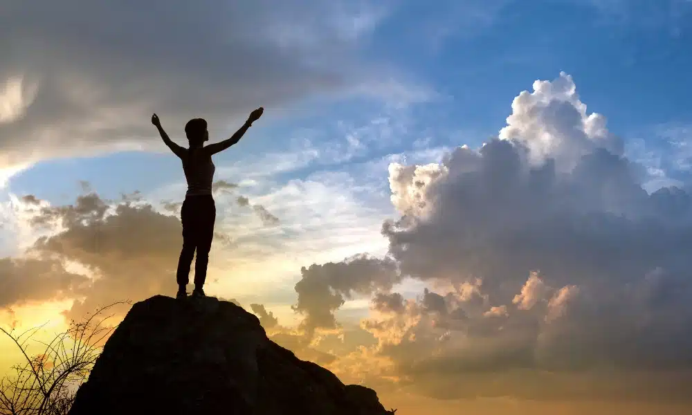 Silhouette einer Frau auf Felsen, die auf Sonnenuntergang blickt.