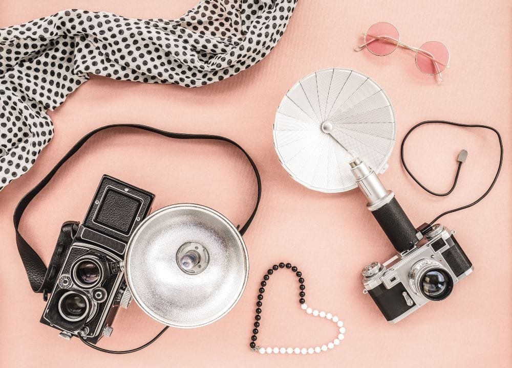 Vintage Fotokameras, Kette und rosa Sonnenbrille auf rosa Hintergrund.