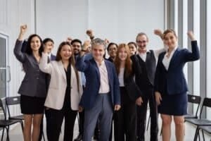 Das Bild zeigt ein motiviertes Team von Geschäftspersonen, die mit erhobenen Fäusten zusammenstehen und Freude ausstrahlen.