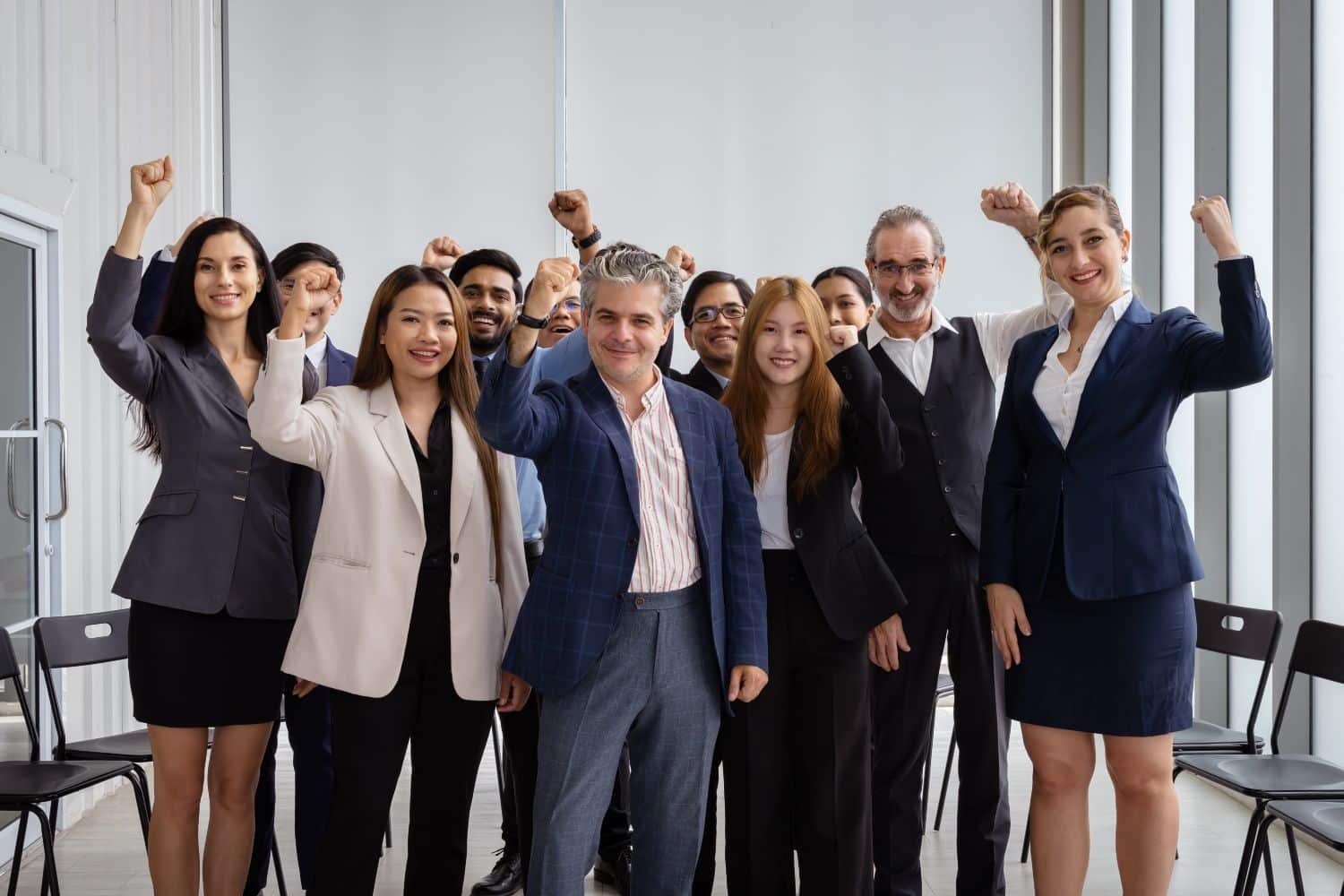 Das Bild zeigt ein motiviertes Team von Geschäftspersonen, die mit erhobenen Fäusten zusammenstehen und Freude ausstrahlen.