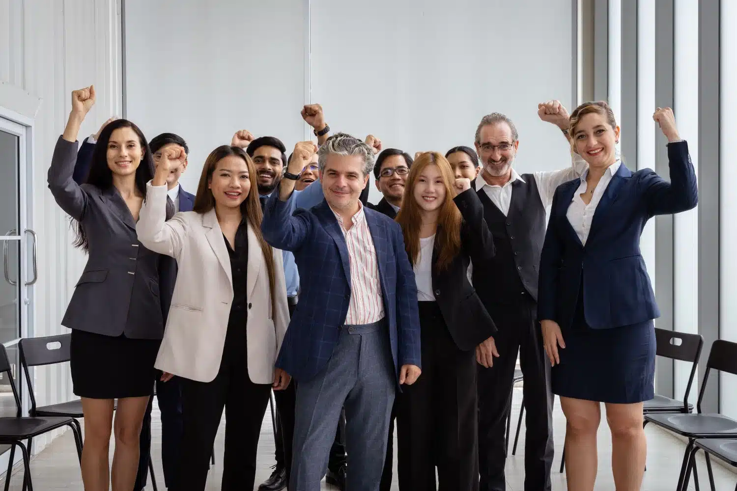 Das Bild zeigt ein motiviertes Team von Geschäftspersonen, die mit erhobenen Fäusten zusammenstehen und Freude ausstrahlen.