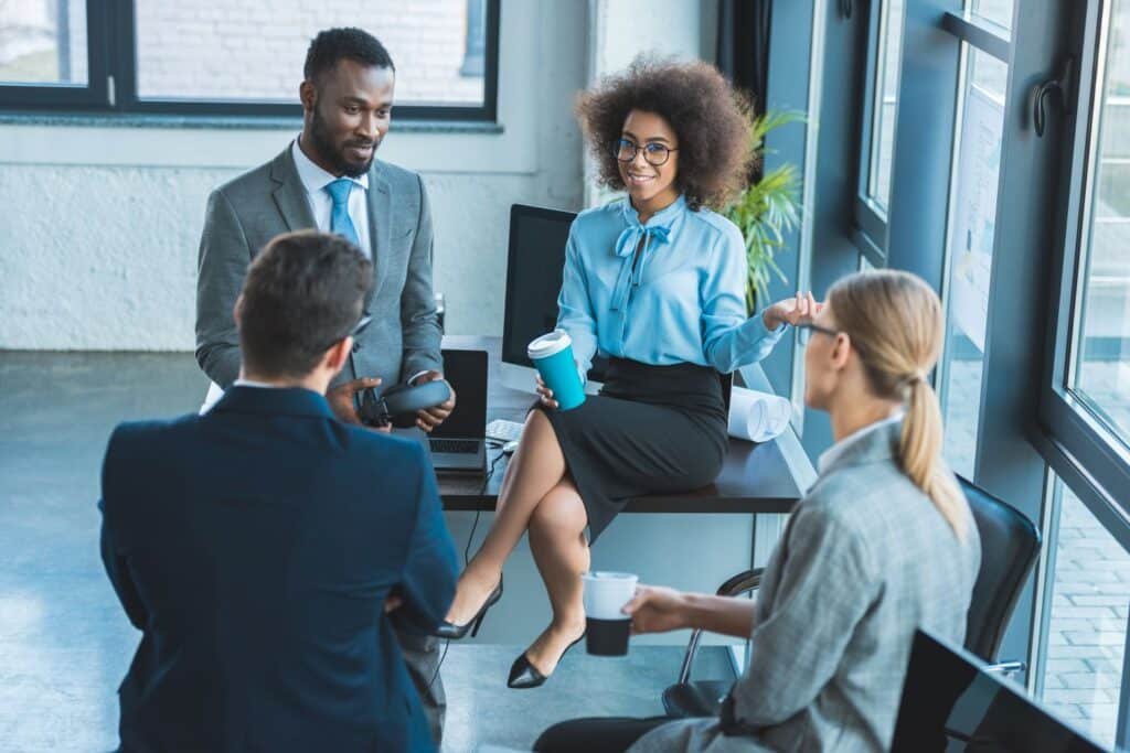 Geschäftsteam in modernem Büro bei informellem Meeting, diskutiert Ideen und hält Kaffeebecher.