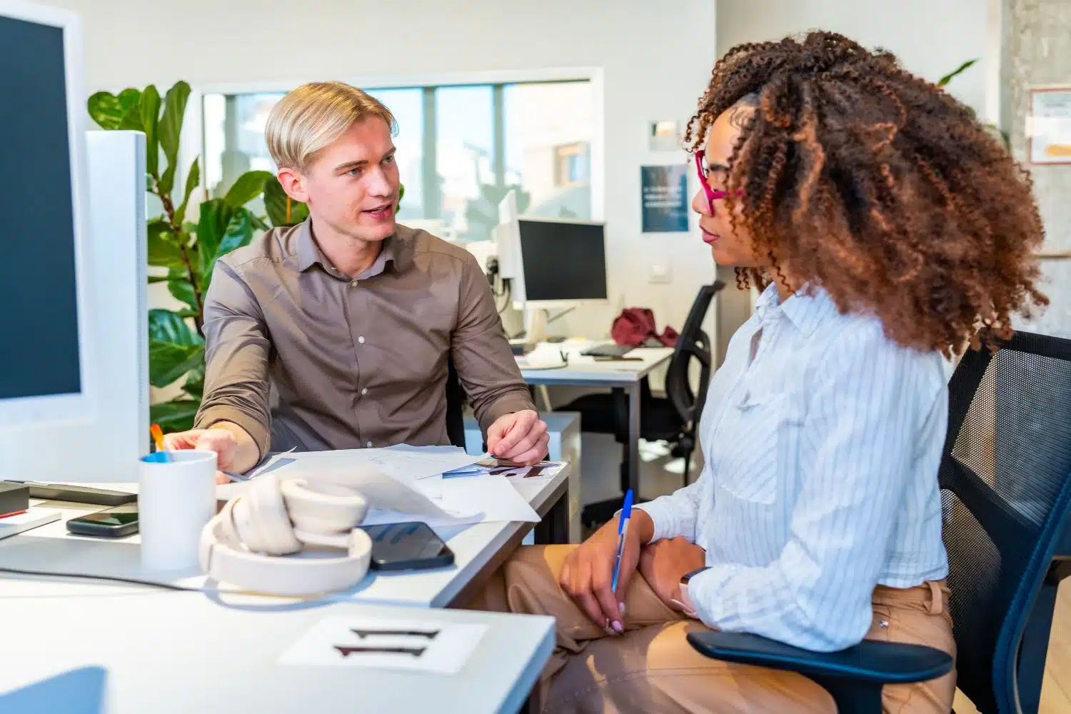 Zwei Kollegen im Büro im Gespräch über Unterlagen und Strategien am Schreibtisch.
