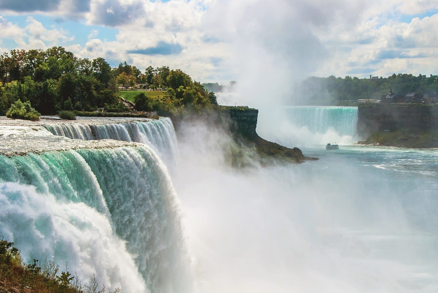 Niagara-Fälle umrandet von grüner Landschaft mit Häusern vereinzelt.