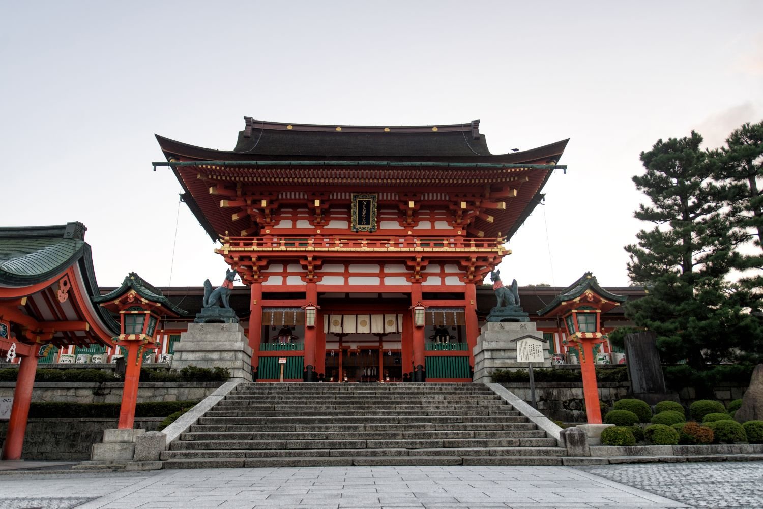 Graue Treppen führen zum Fushimi-Inari-Schrein, Bäume und blauer Himmel im Hintergrund.